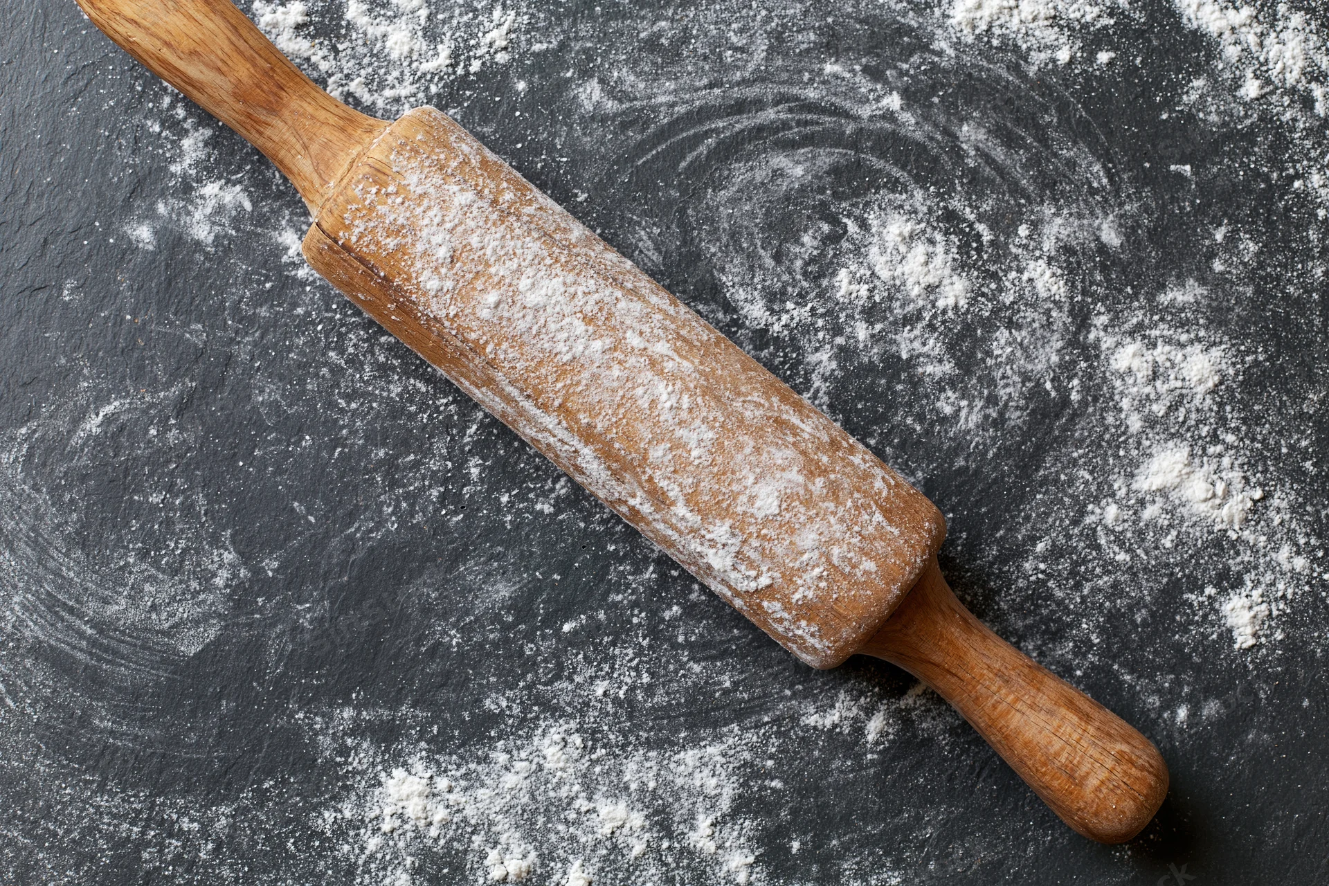 Wooden rolling pin dusted with flour on dark textured countertop