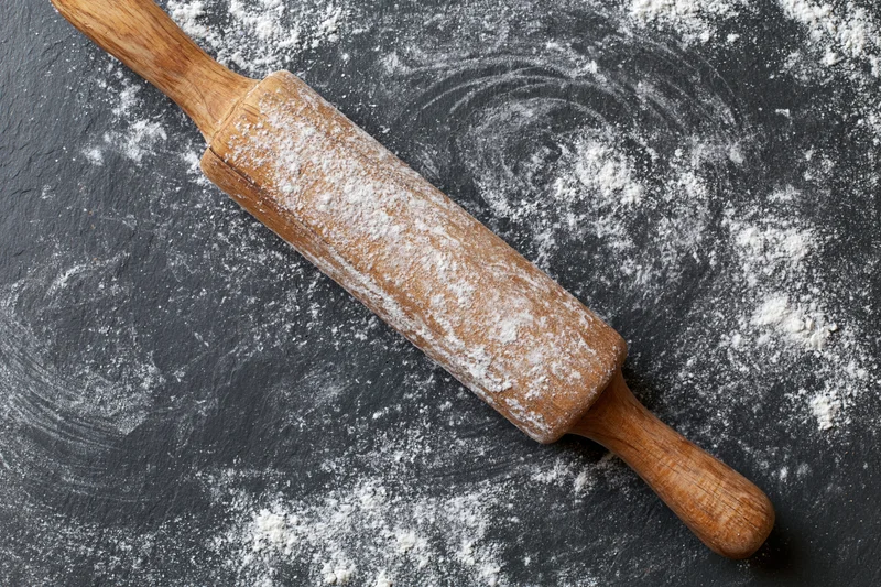 Wooden rolling pin dusted with flour on dark textured countertop