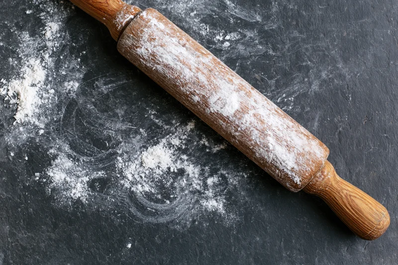 Wooden rolling pin dusted with flour on dark slate countertop