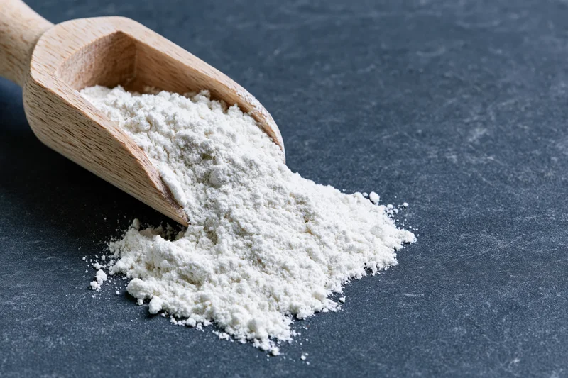 Wooden scoop pouring white flour onto dark slate surface