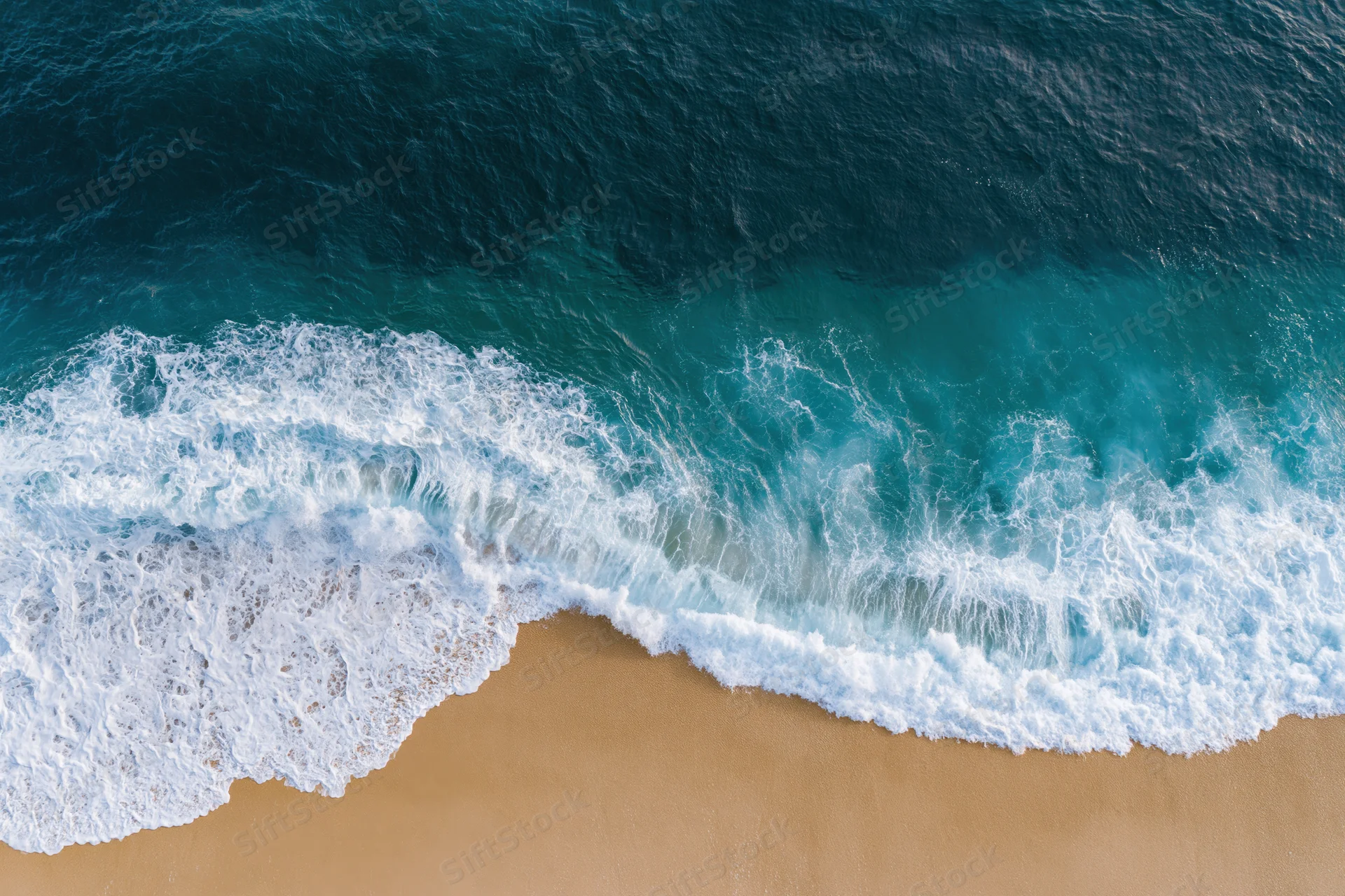 Waves breaking on sandy beach from overhead view