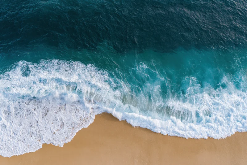 Waves breaking on sandy beach from overhead view