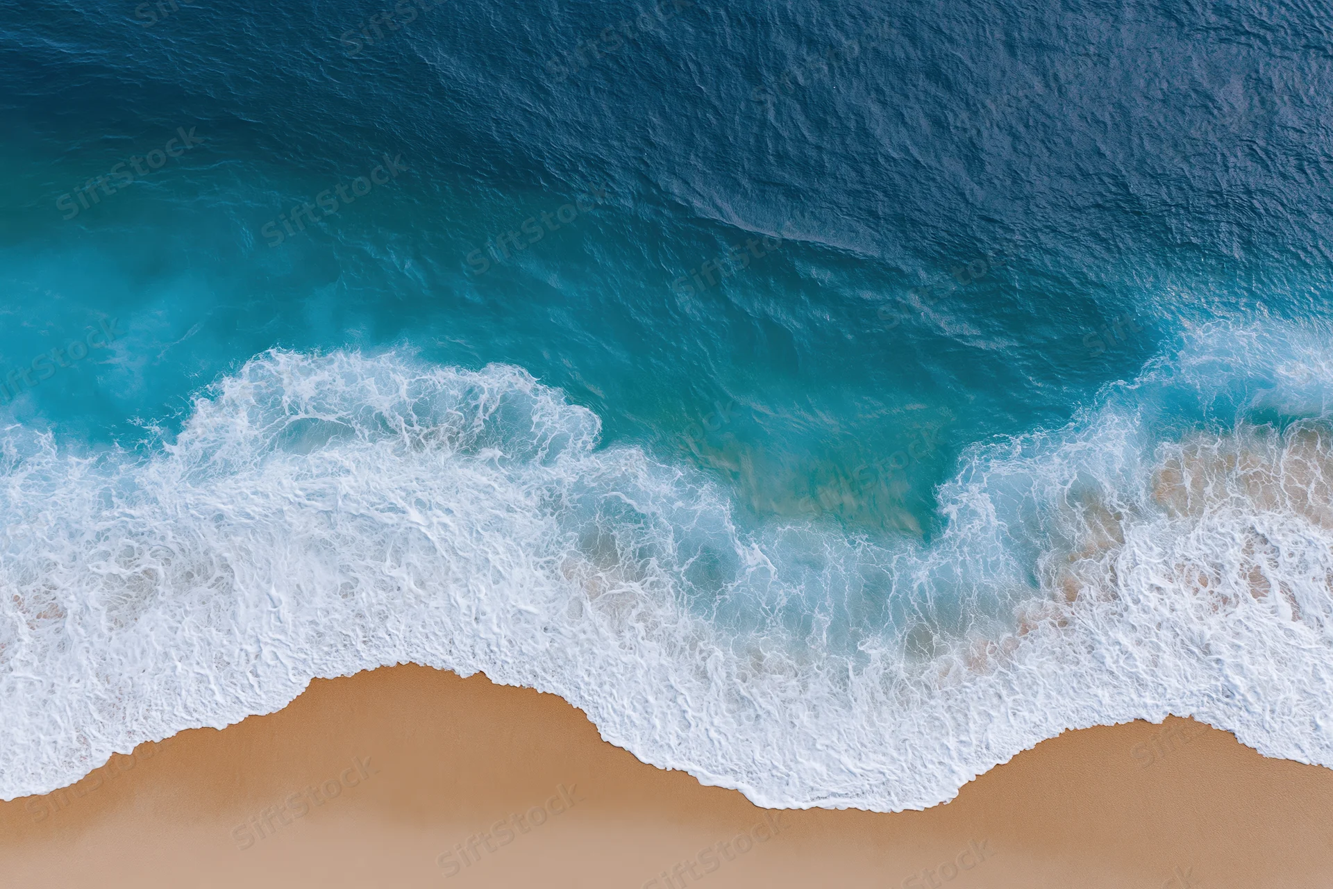 Waves breaking on sandy beach from overhead view