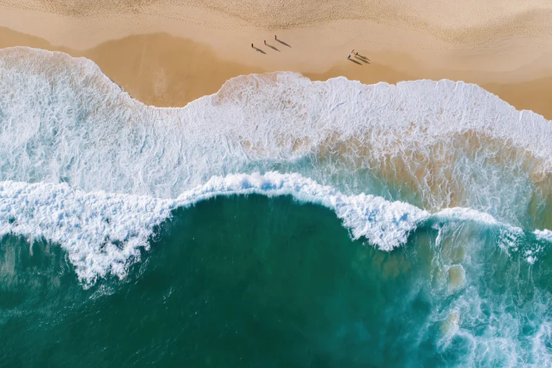Aerial view of waves breaking on a sandy beach with people walking along the shore