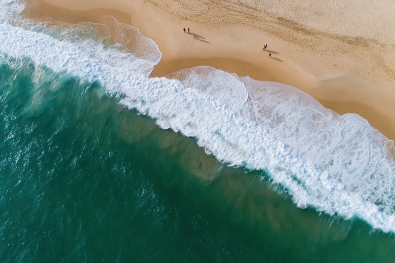 Aerial view of waves breaking on a sandy beach with people walking along the shore
