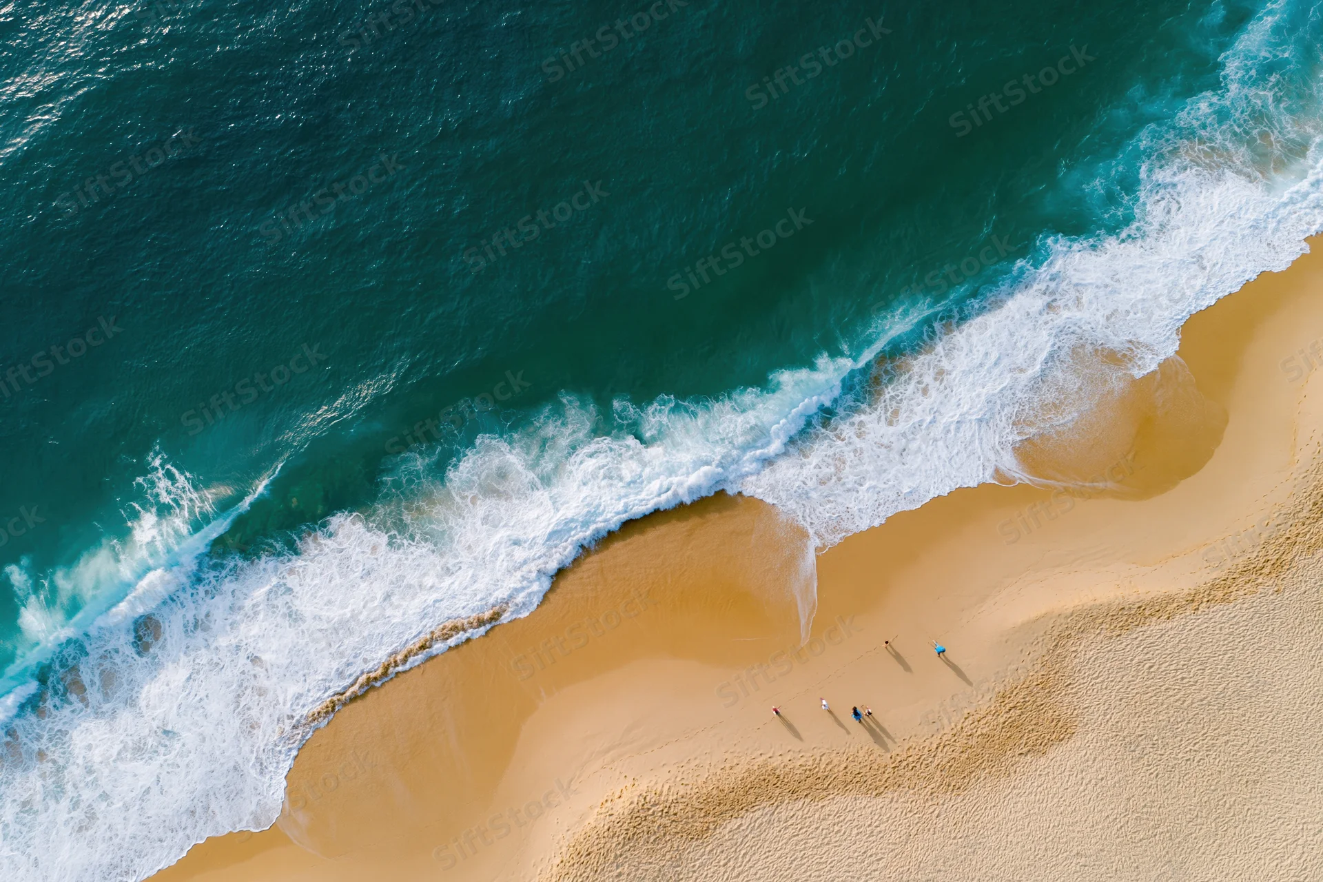 Aerial view of waves breaking on a sandy beach with people walking along the shore