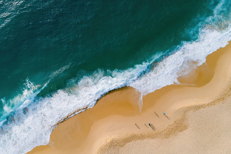 Aerial view of waves breaking on a sandy beach with people walking along the shore