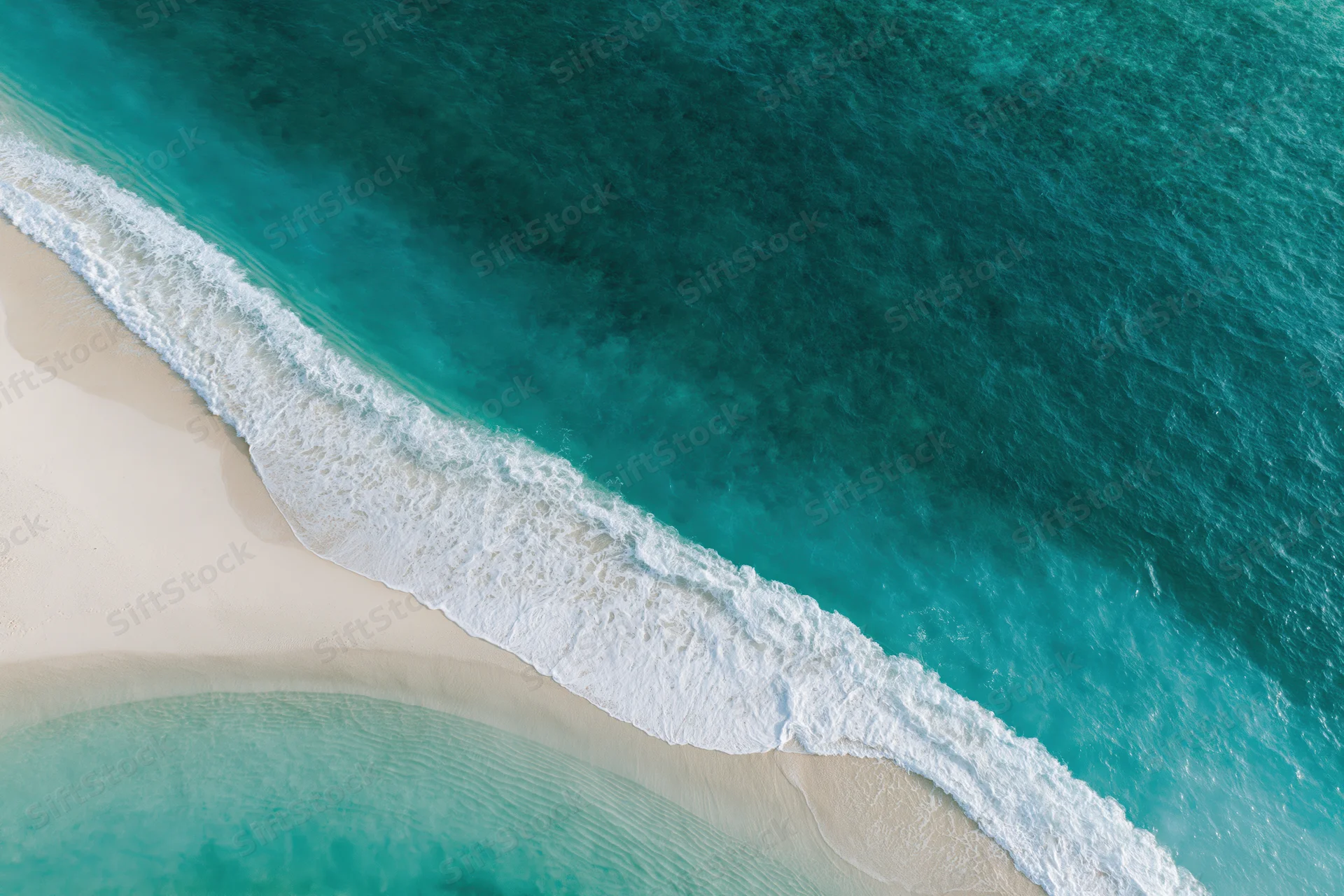 Aerial view of turquoise ocean waves meeting white sand beach