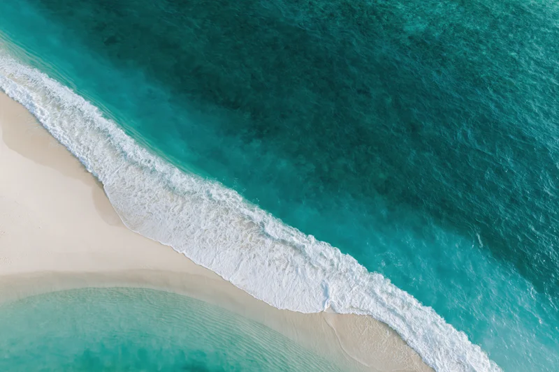 Aerial view of turquoise ocean waves meeting white sand beach