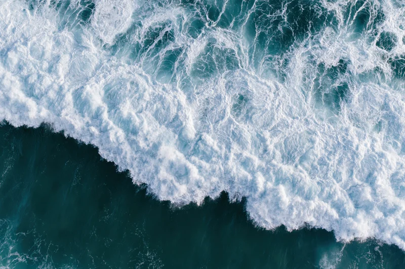 Aerial view of a breaking ocean wave with white foam and deep blue water