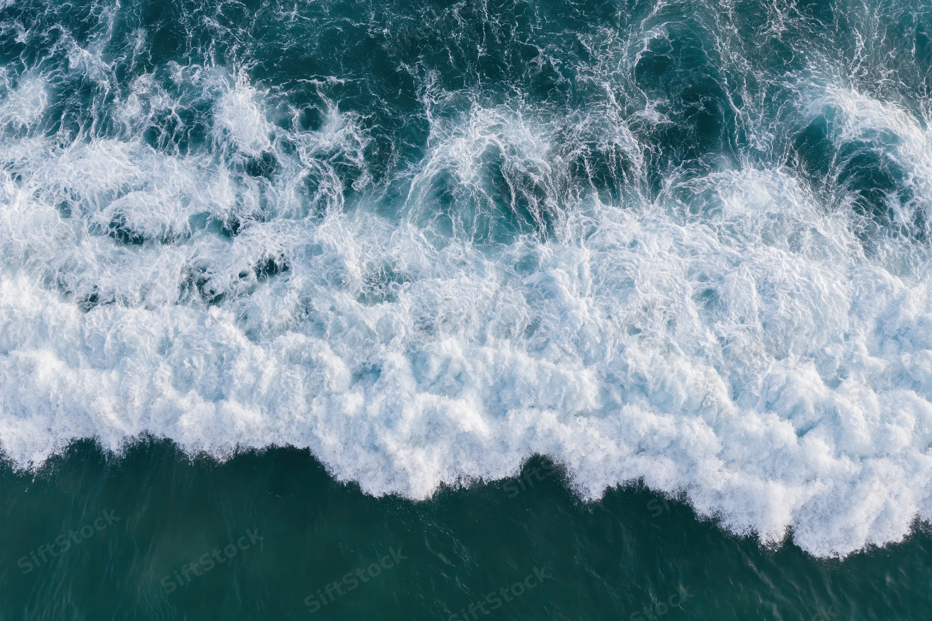 Aerial view of breaking ocean waves with white foam and deep blue water