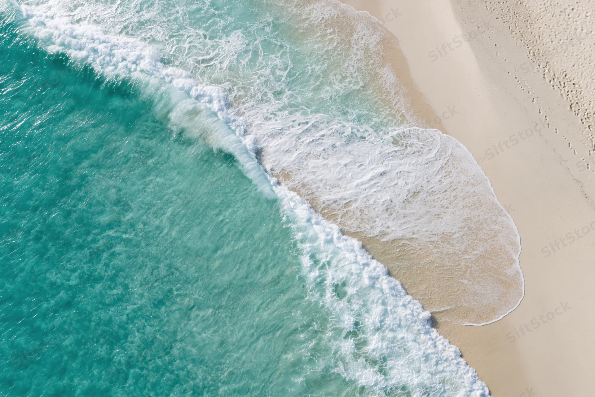 Aerial view of turquoise ocean waves breaking on a sandy beach