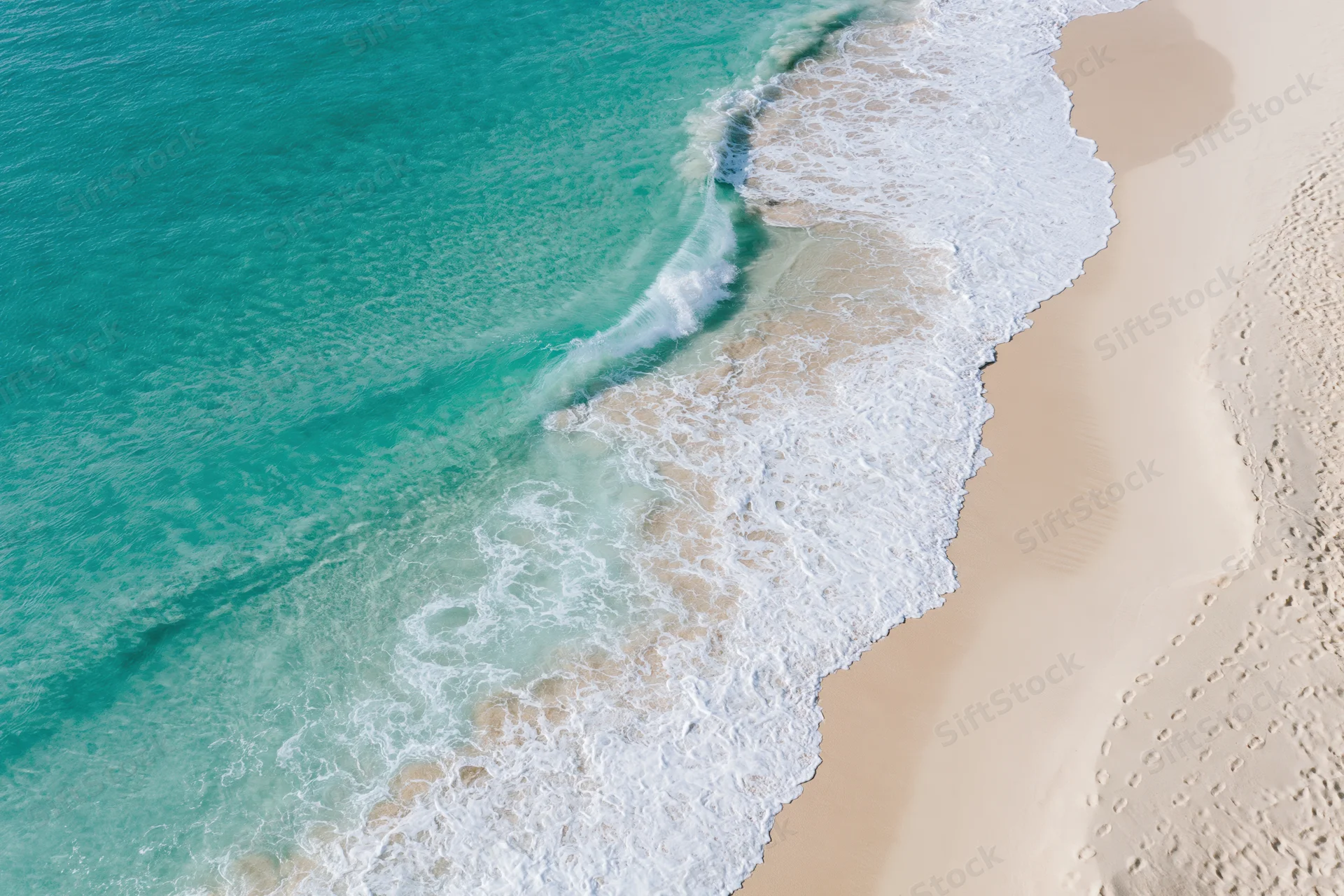 Aerial view of turquoise ocean waves meeting white sandy beach