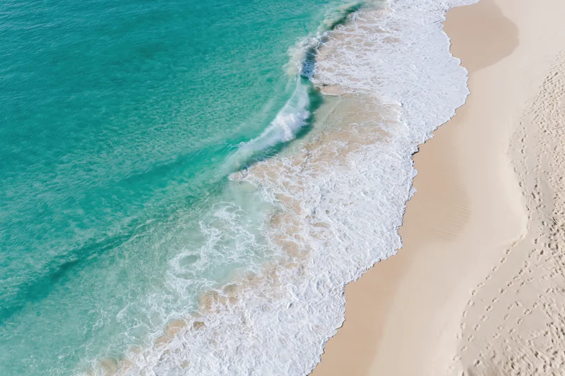 Aerial view of turquoise ocean waves meeting white sandy beach