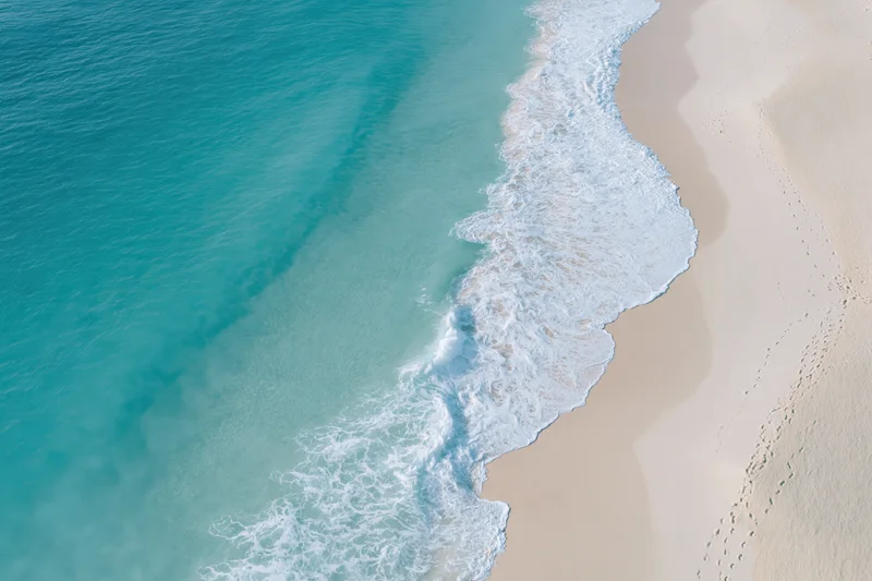 Aerial view of turquoise ocean waves breaking on a sandy beach shoreline