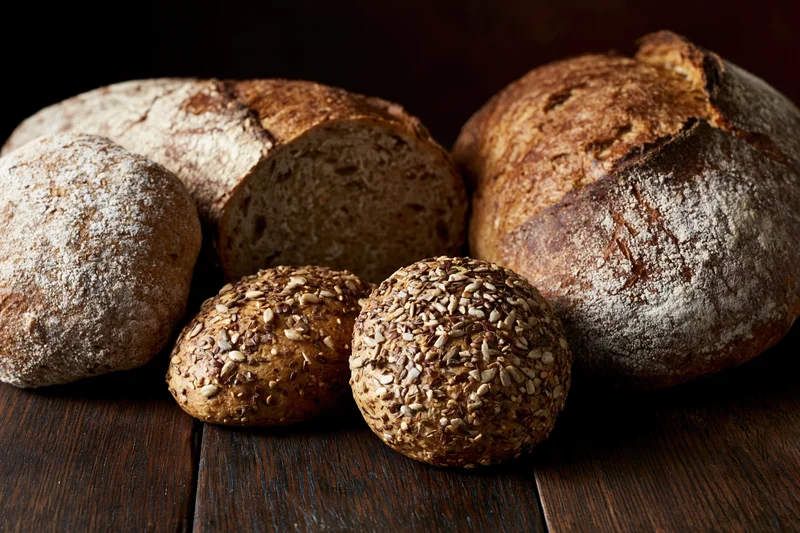 Several loaves of artisan bread with sesame seeds and flour dusting arranged on a dark wooden table