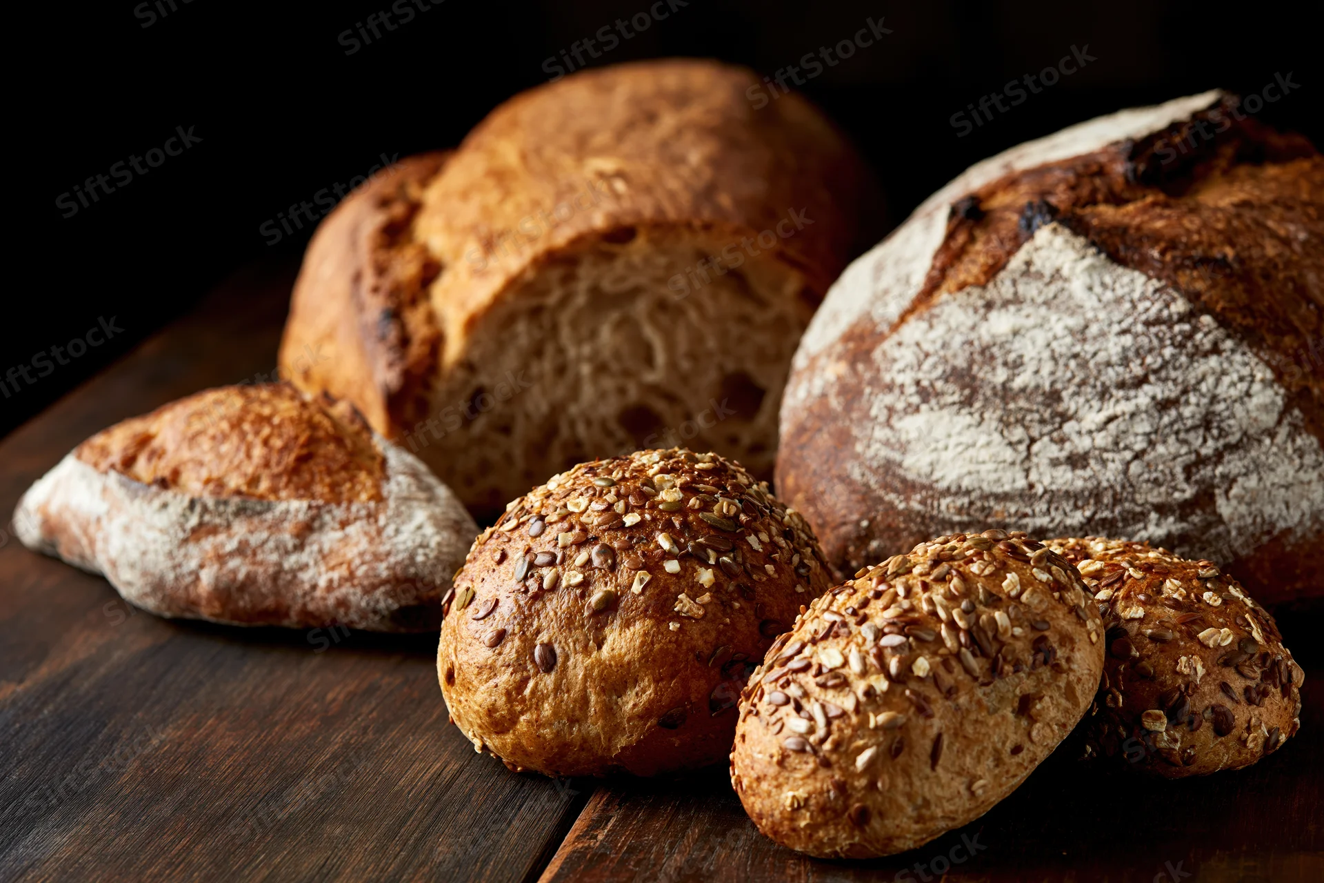 Assorted artisan bread loaves and seeded rolls arranged on a dark wooden table