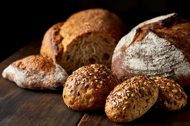 Assorted artisan bread loaves and seeded rolls arranged on a dark wooden table