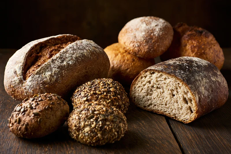 Various artisan bread loaves and seeded rolls arranged on a dark wooden table