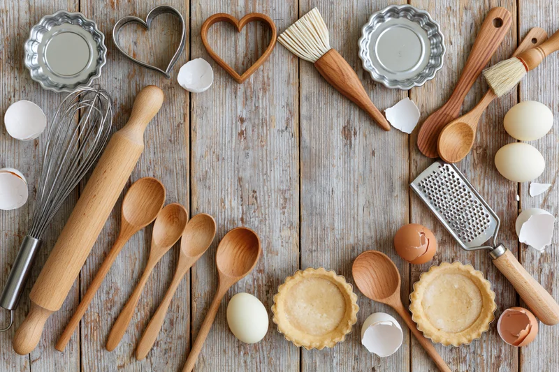 Baking utensils and ingredients arranged on a wooden table in a flat lay overhead view