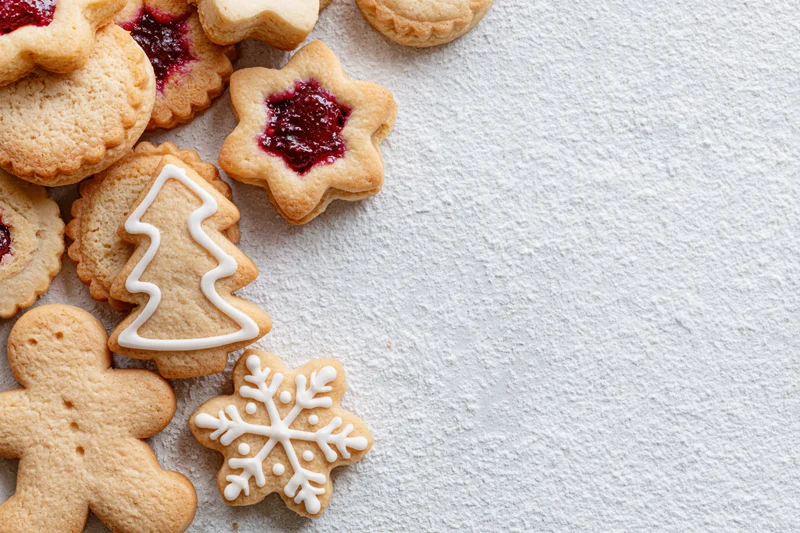 Christmas cookies shaped like trees, snowflakes, and gingerbread men with jam and icing on a white textured surface