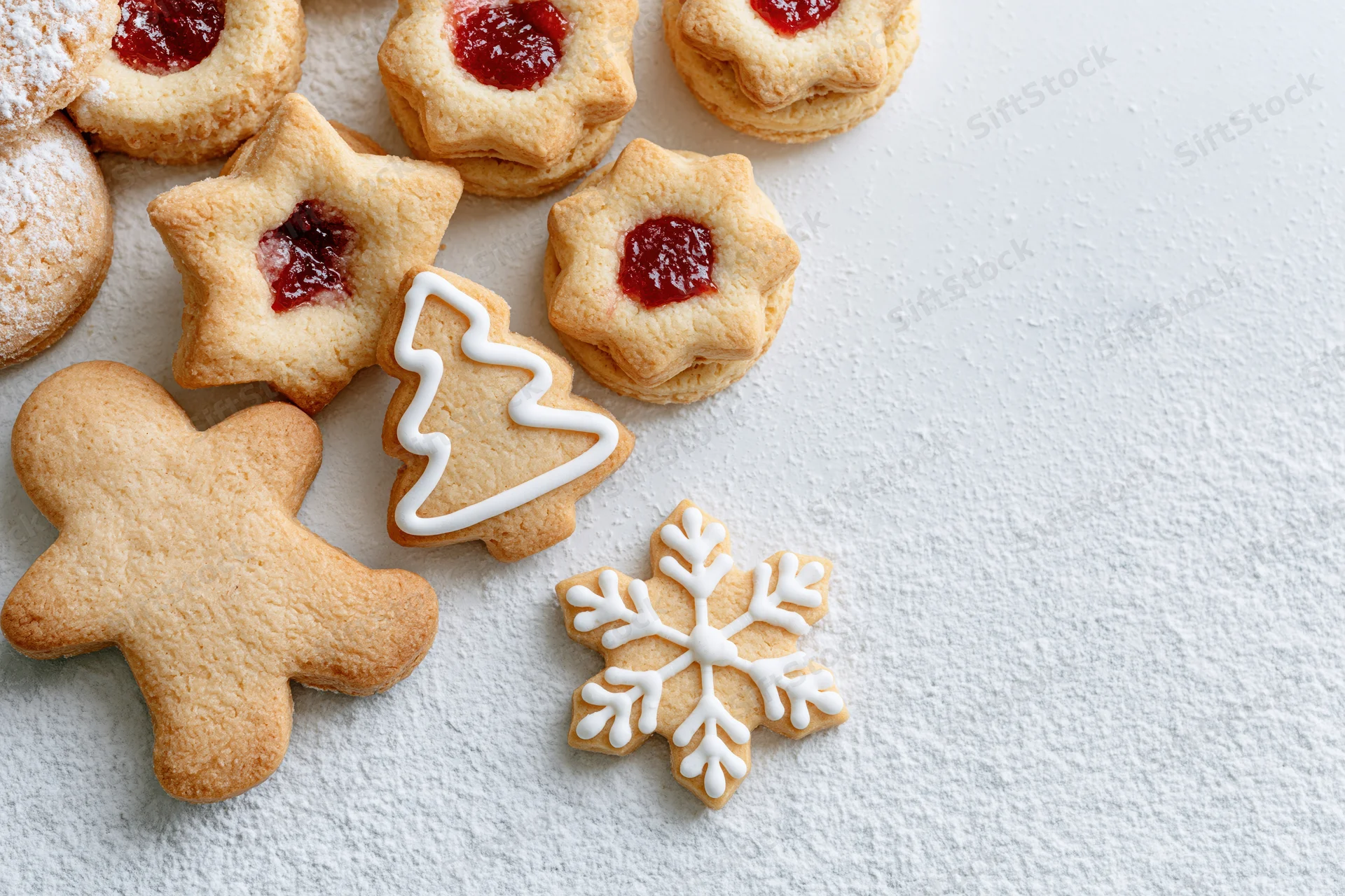 Assorted christmas cookies shaped as stars, trees, snowflakes and gingerbread men with jam and icing on a white textured surface