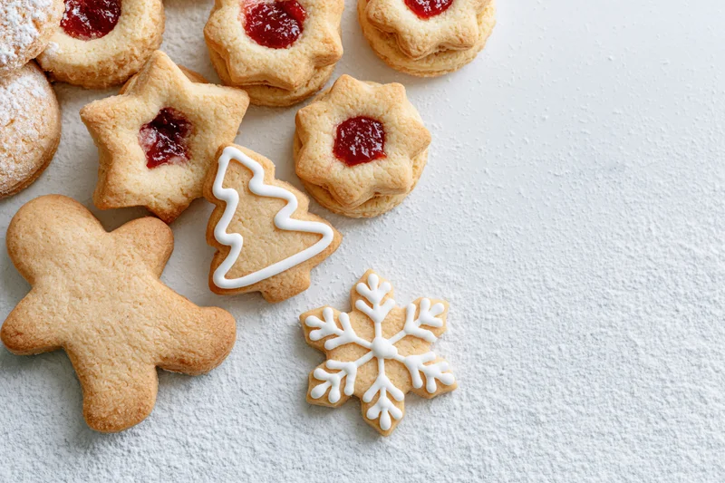 Assorted christmas cookies shaped as stars, trees, snowflakes and gingerbread men with jam and icing on a white textured surface