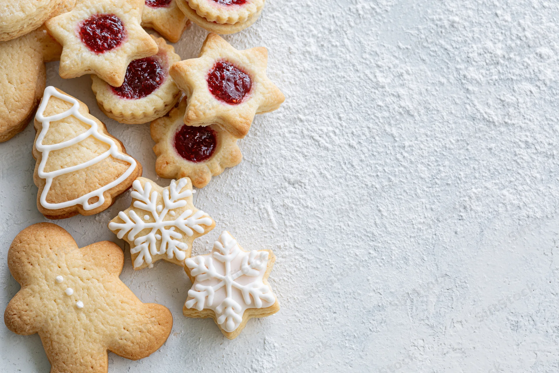 Christmas cookies shaped as gingerbread men, stars, trees and snowflakes with red jam and white frosting arranged on a light textured surface
