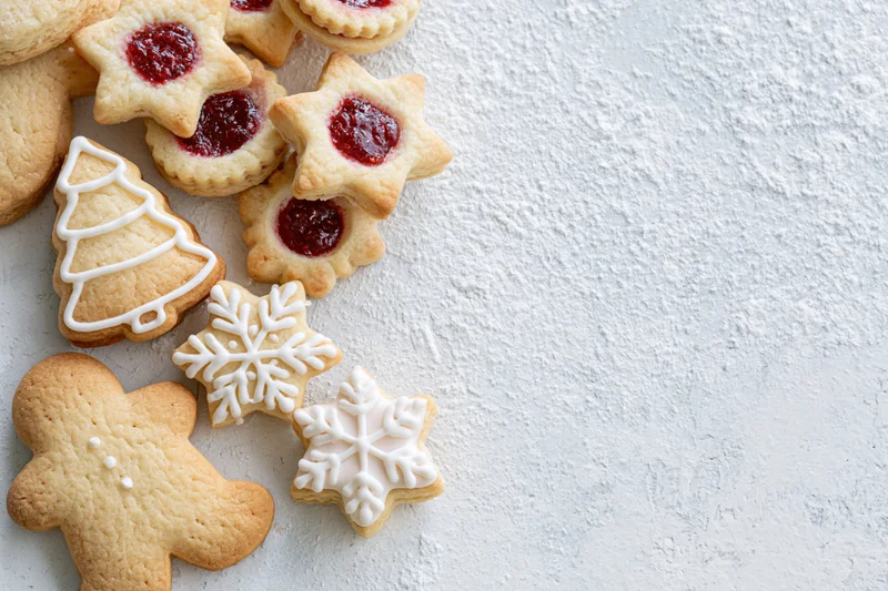 Christmas cookies shaped as gingerbread men, stars, trees and snowflakes with red jam and white frosting arranged on a light textured surface
