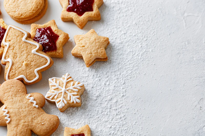 Gingerbread cookies shaped as stars, snowflakes and trees with white icing and red jam on a powdered sugar surface