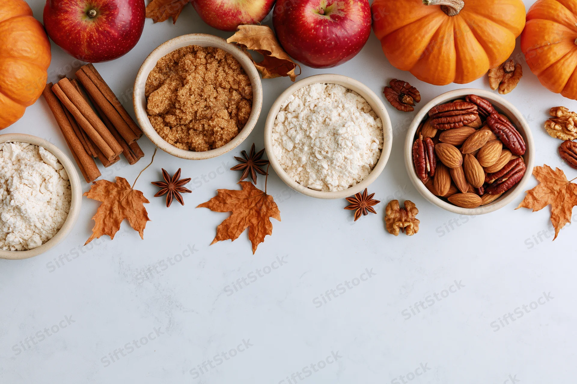 Autumn ingredients arranged on a white marble surface with pumpkins, apples, nuts, spices and leaves for baking