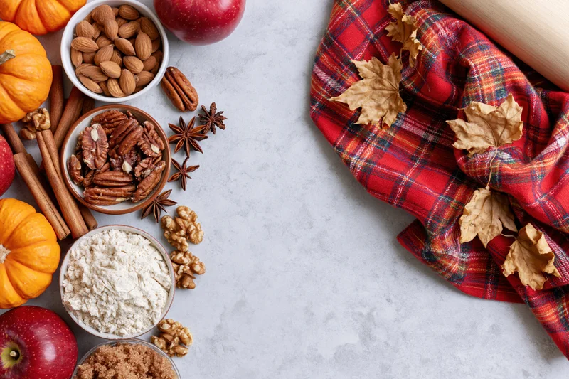 Autumn baking ingredients arranged on countertop with plaid cloth and leaves