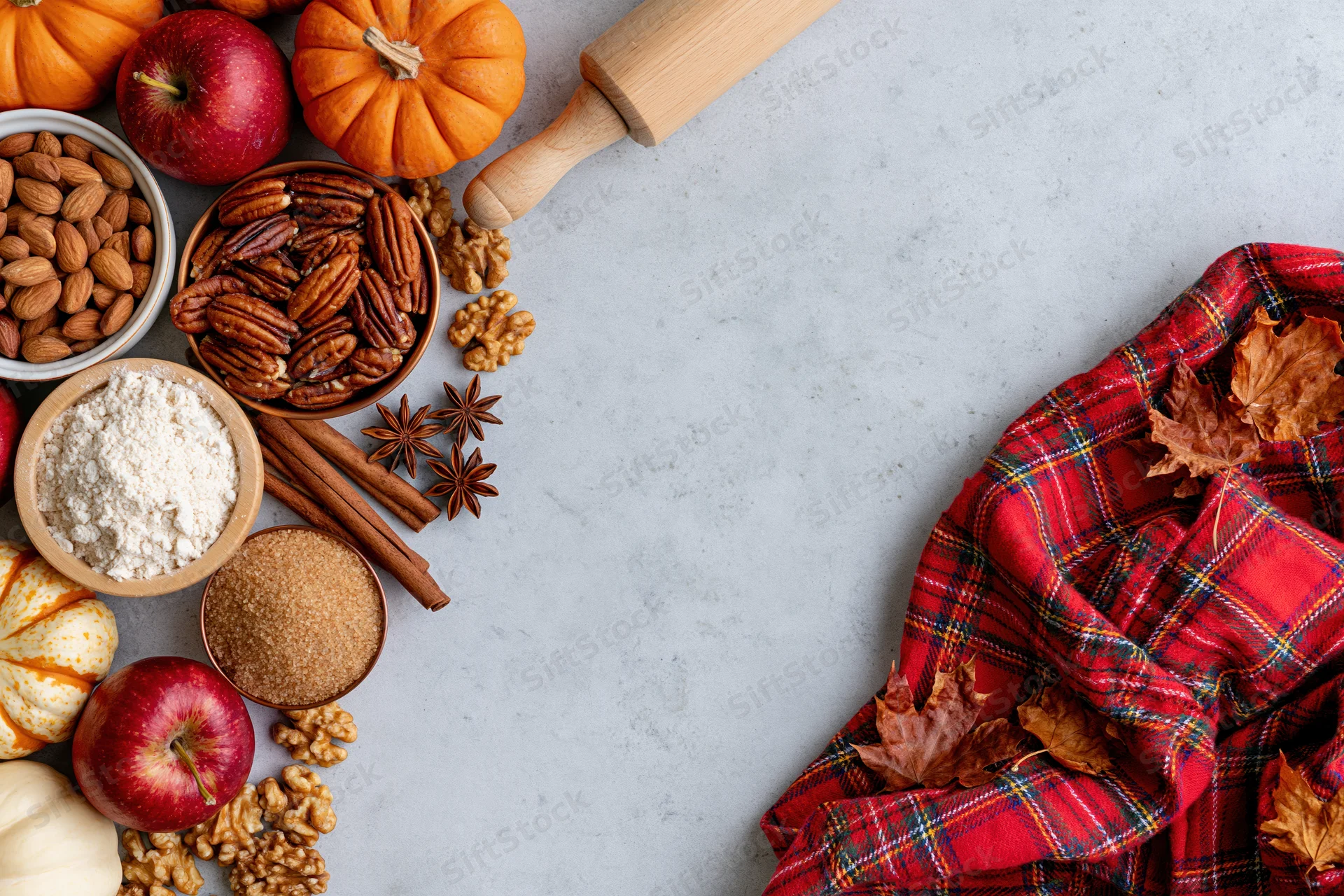 Autumn baking ingredients arranged on marble countertop with plaid scarf and fall leaves