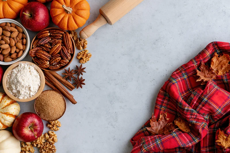 Autumn baking ingredients arranged on marble countertop with plaid scarf and fall leaves