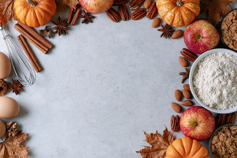 Autumn baking ingredients arranged in a frame around a white countertop with copyspace