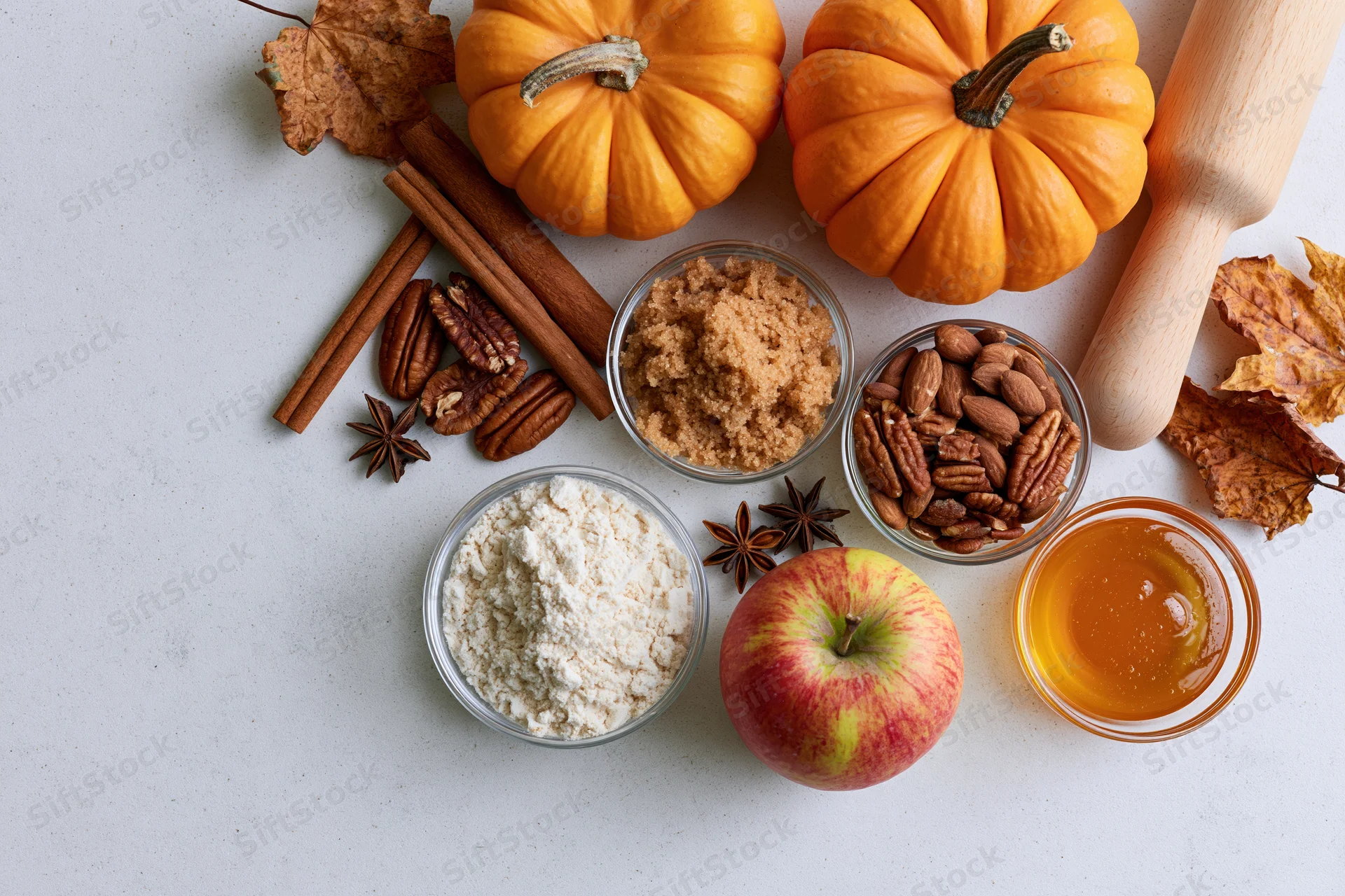 Pumpkin and apple baking ingredients arranged on a countertop with autumn leaves and a rolling pin