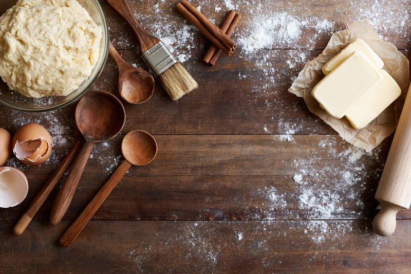 Baking ingredients arranged on a wooden table with flour dusting and copyspace