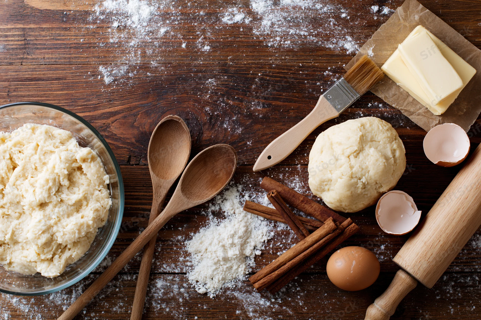 Dough and baking ingredients arranged on a wooden table with utensils and spices