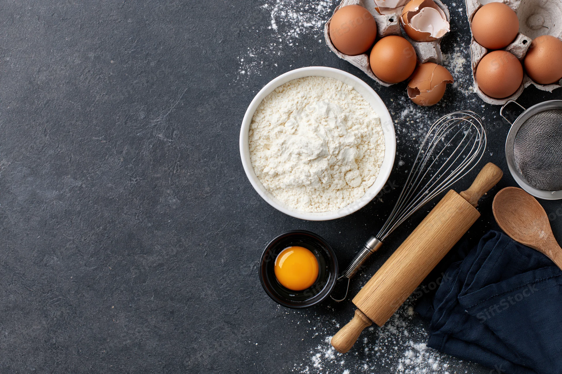 Baking ingredients and tools arranged on dark countertop with copyspace