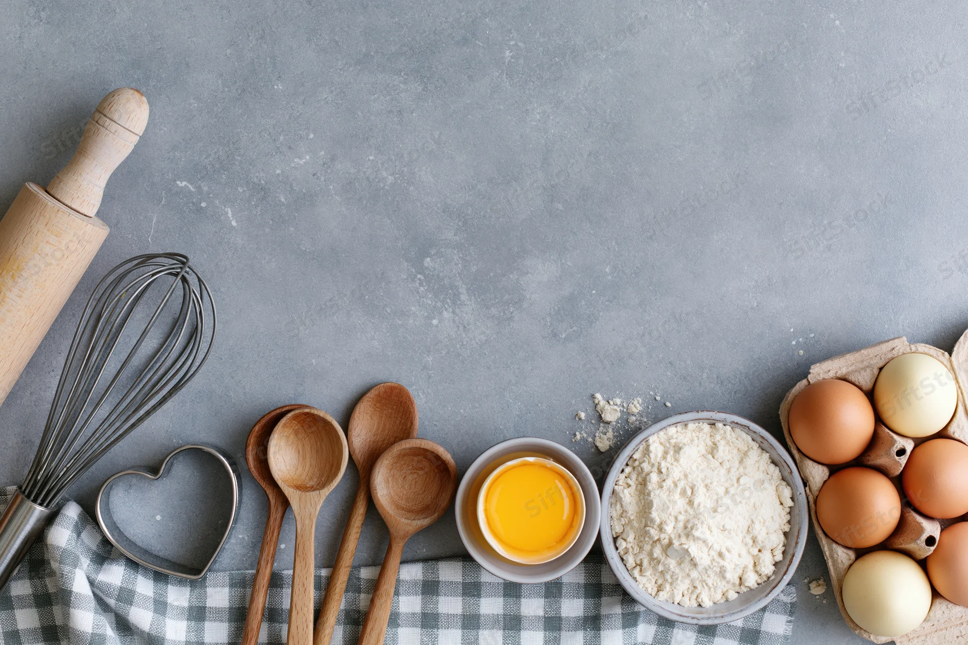 Baking ingredients and tools arranged on a gray countertop with checkered cloth and copyspace