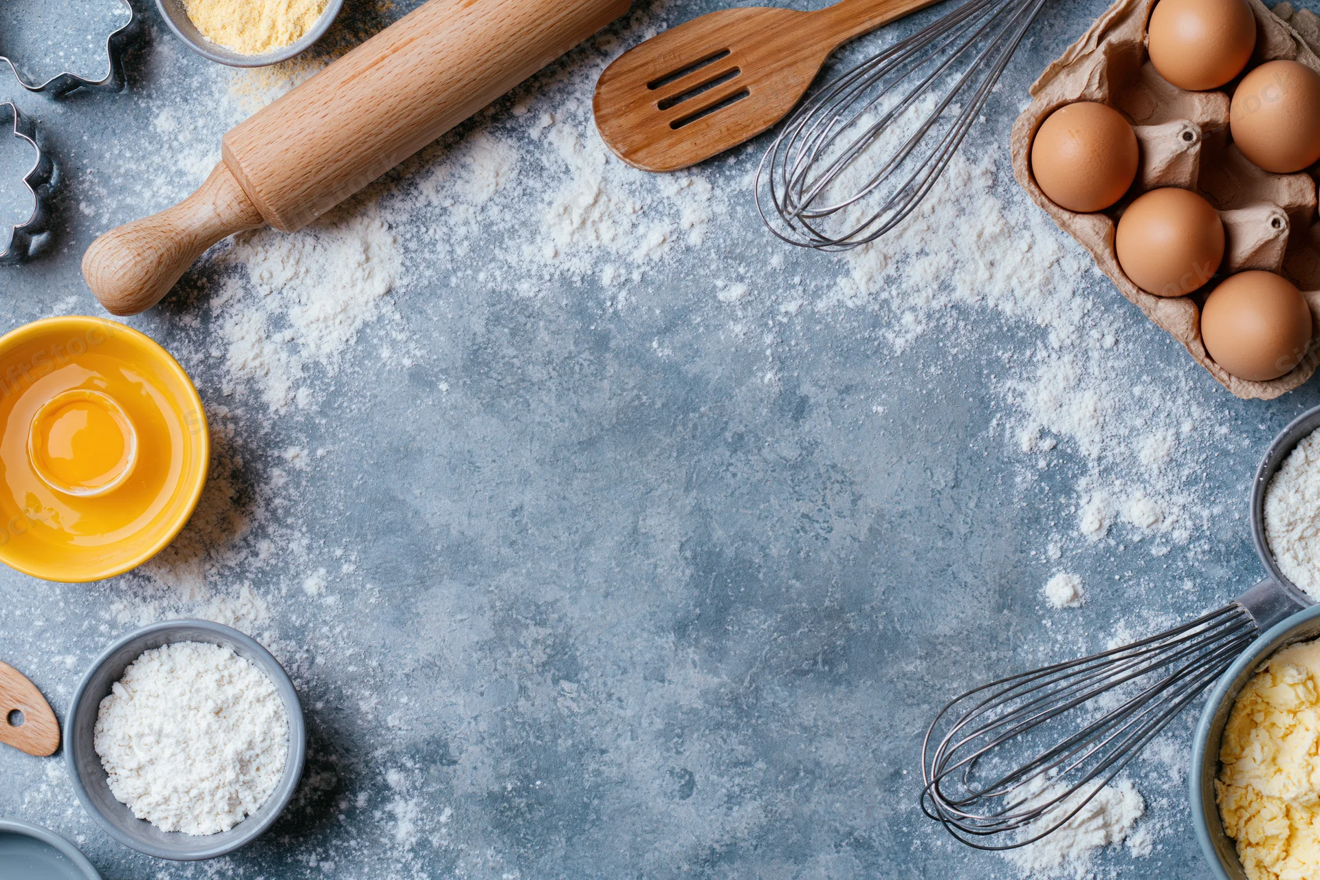 Baking ingredients and tools arranged on a floured gray countertop with copyspace in center