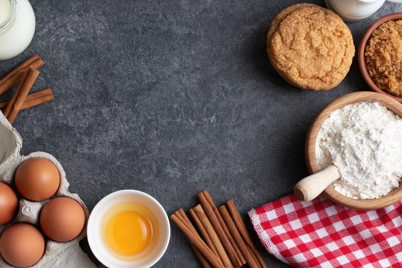 Baking ingredients arranged around a dark countertop with copyspace in center