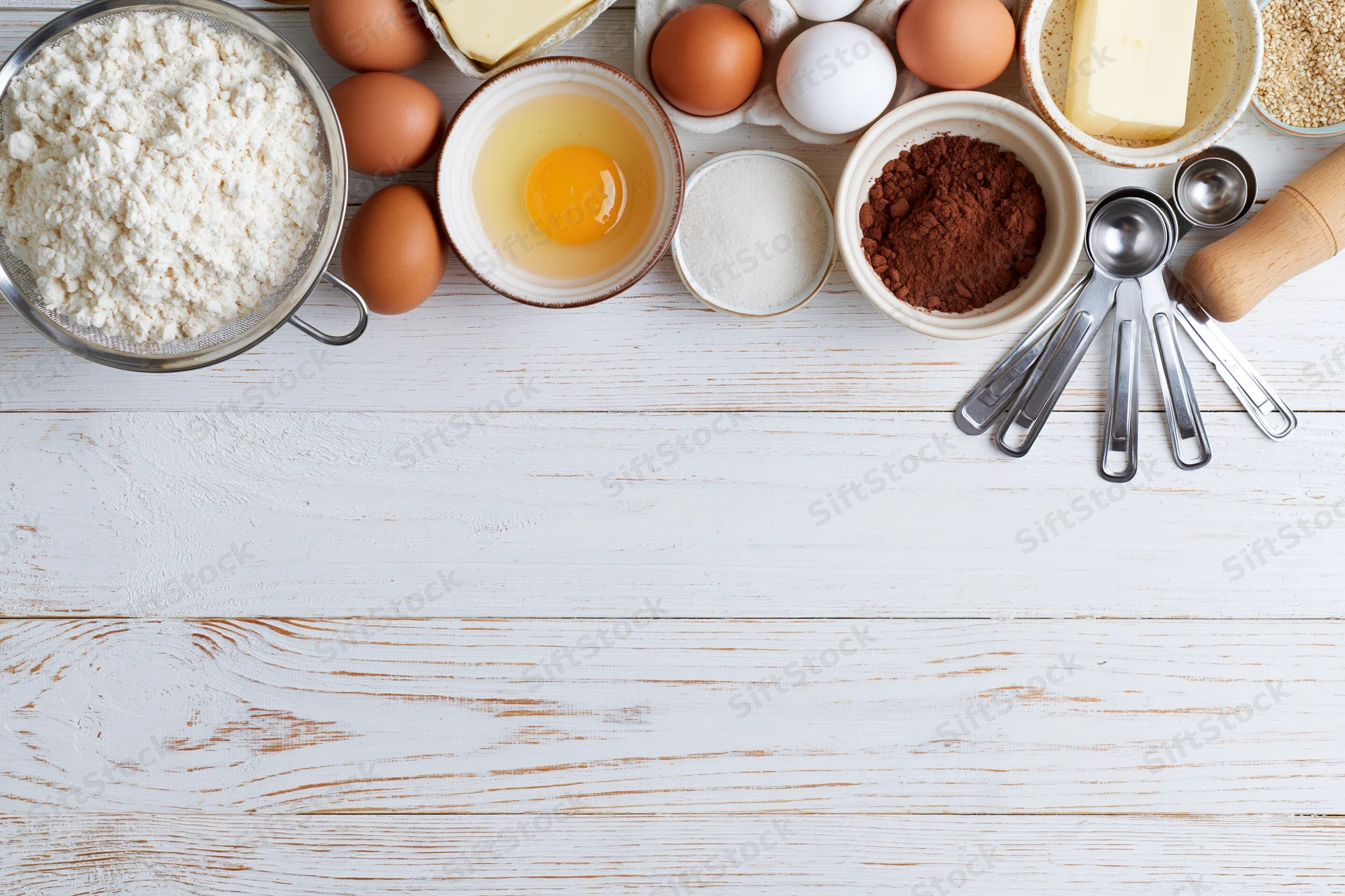 Baking ingredients arranged on white wooden surface with copyspace below