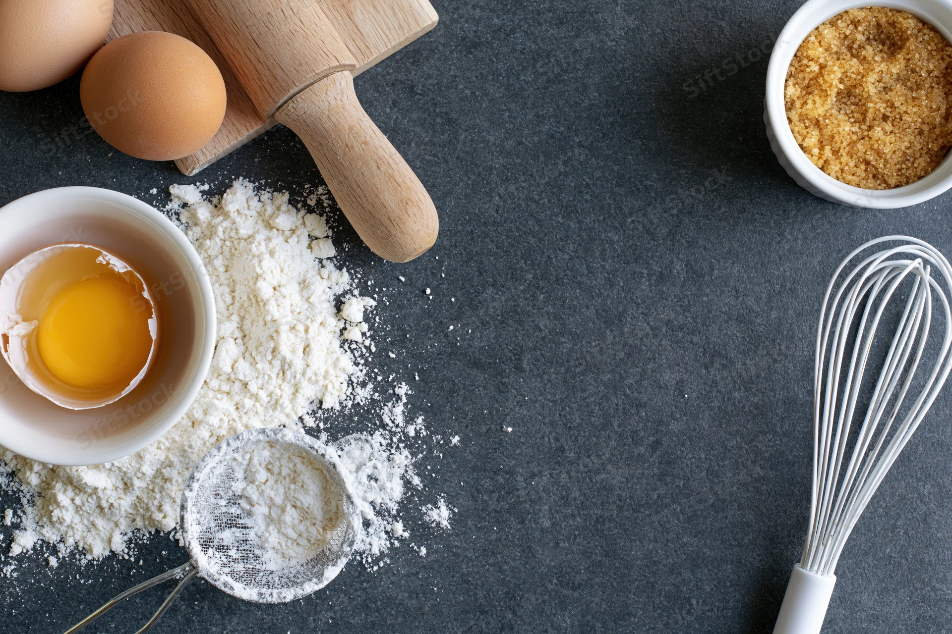 Baking ingredients and tools arranged on dark countertop with copyspace
