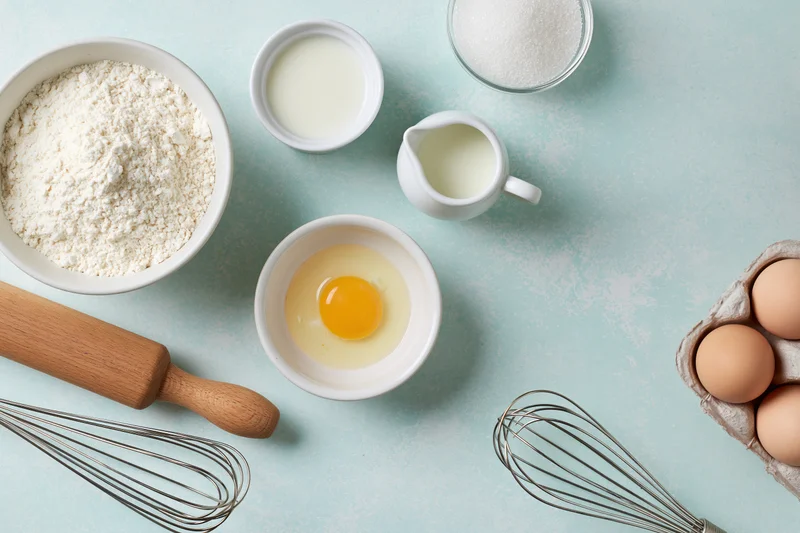 Baking ingredients arranged on a light blue surface with utensils and bowls
