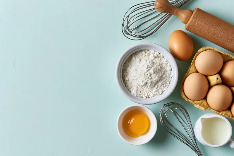 Baking ingredients arranged on a light blue surface with copyspace on the left