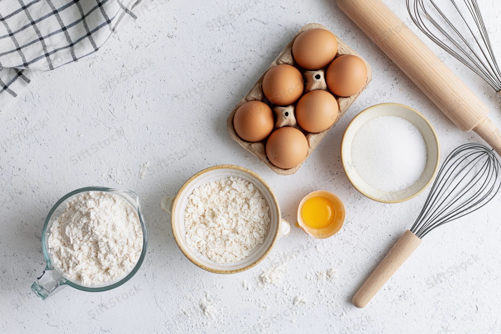 Baking ingredients arranged on a white countertop with utensils and bowls