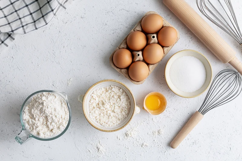 Baking ingredients arranged on a white countertop with utensils and bowls
