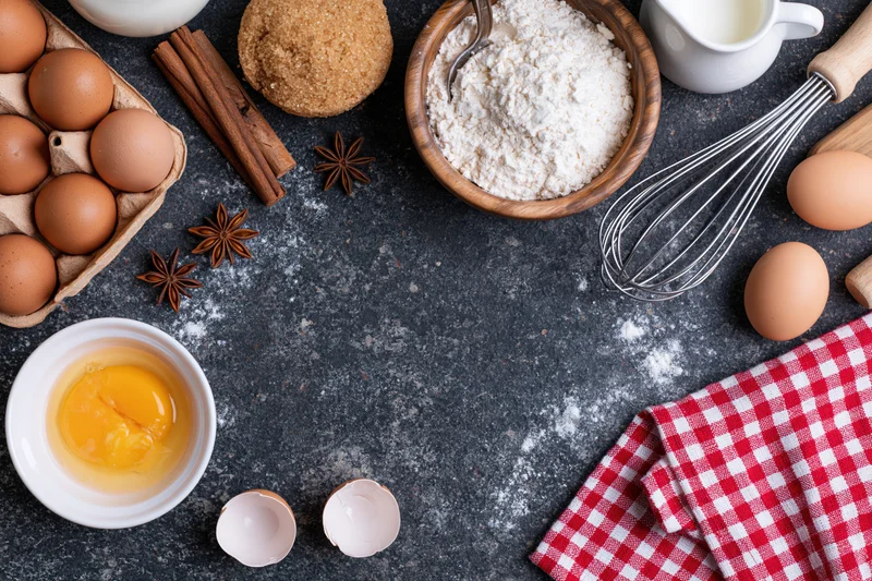 Baking ingredients arranged on dark countertop with red checkered cloth and copyspace