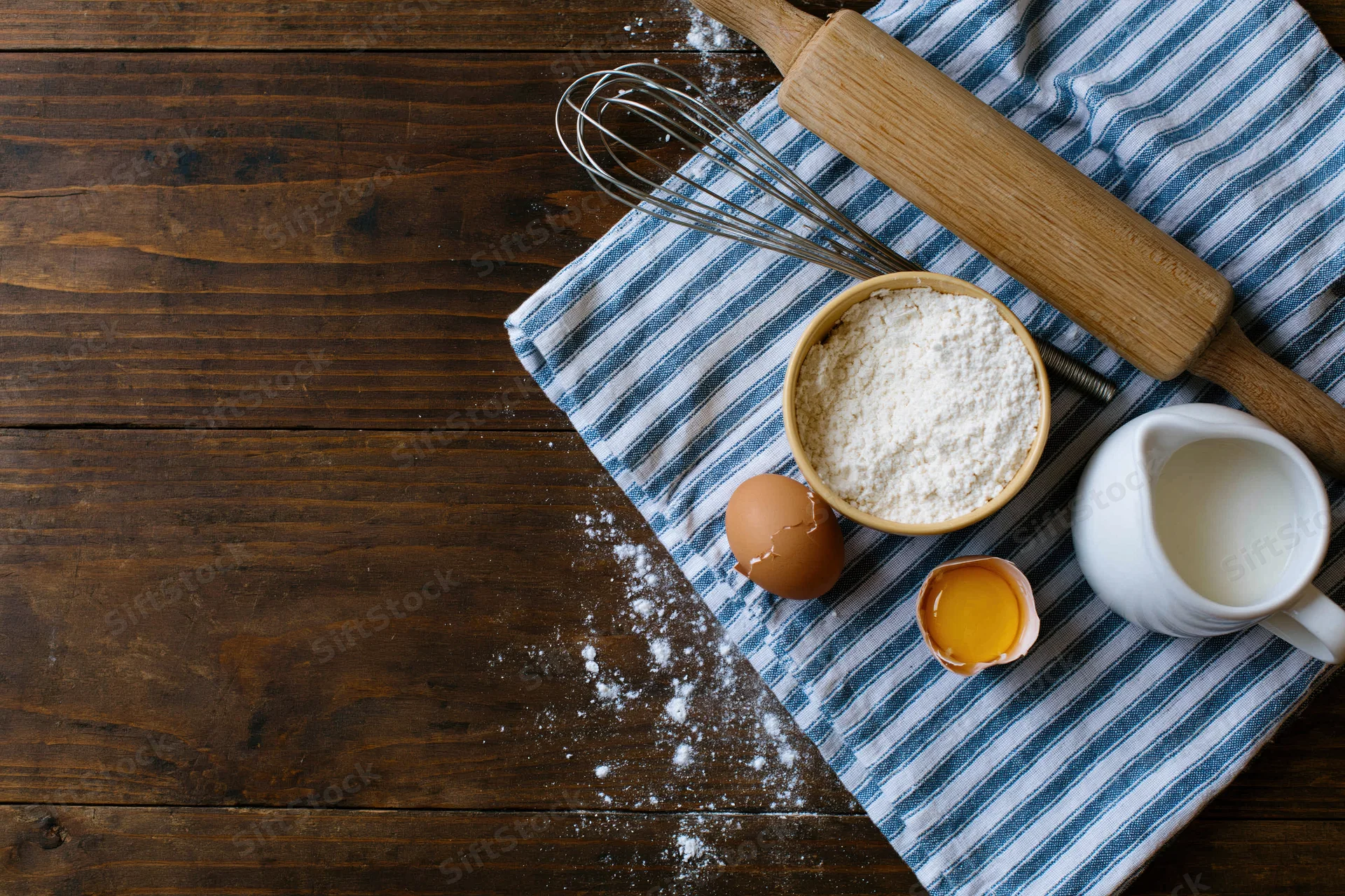Baking ingredients arranged on a striped cloth over a wooden table with copyspace on the left